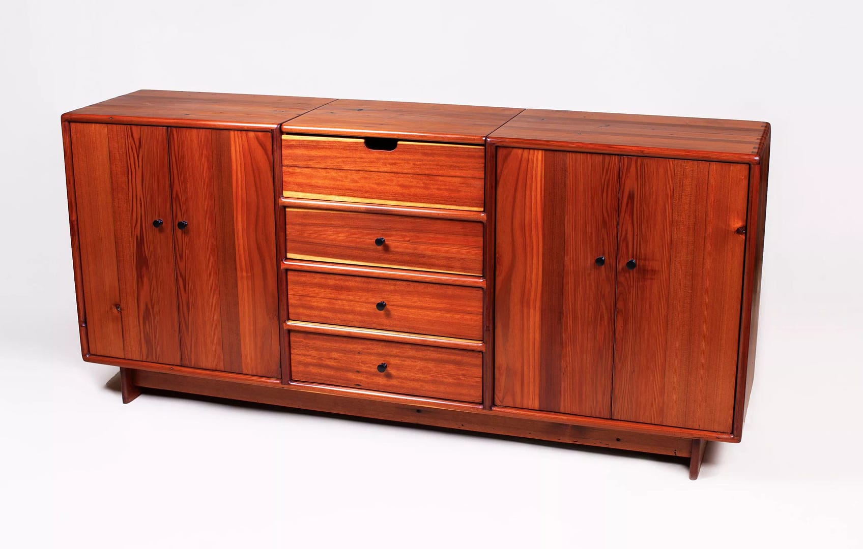 Front view of a solid redwood credenza with 3 drawers in the center and a storage cabinet on either side of the drawers. The piece can function as a sideboard or turntable cabinet. It has a lift top opening in the top to hold either serving accoutrement or a turntable. Built using hand-tools from solid redwood with pine sided drawers, by Marc Springer woodworker and furniture maker.