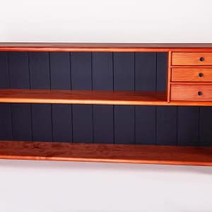 A low profile, free-standing redwood bookcase with two-shelves and three drawers. The middle shelf of the bookcase has 3 small drawers on the left hand side. The bookcase has a satin sheen and you can see that the back of the shelves behind the books is a solid black matte finish. It is a long bookcase with a low profile. It is 58" wide, 10 1/2 deep and 29" tall. this bookcase was milled, joined and crafted using only hand tools and traditional wood joinery. It has 5 coats of hand rubbed finish for a satin sheen. The piece was designed and crafted by Marc Springer a furniture maker in Woodland Hills, California.