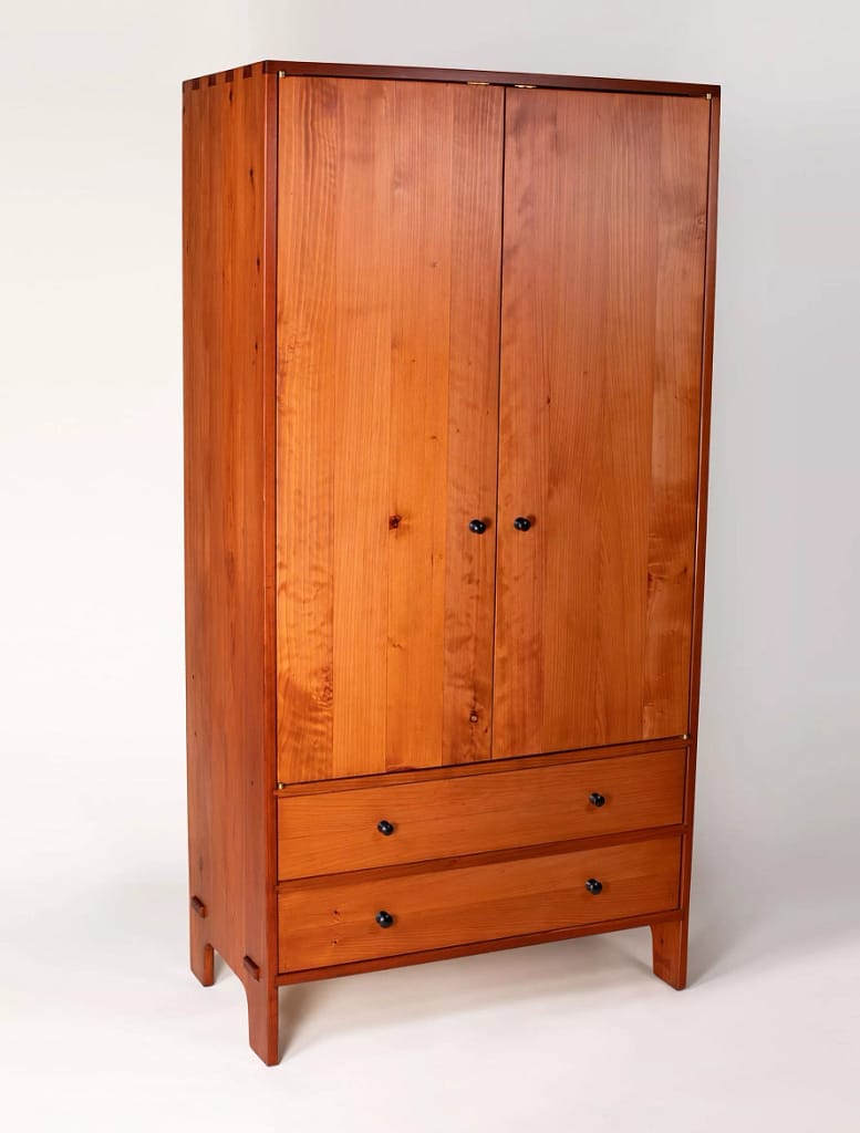 A large, solid wood armoire with hanging space above and two drawers on the bottom.